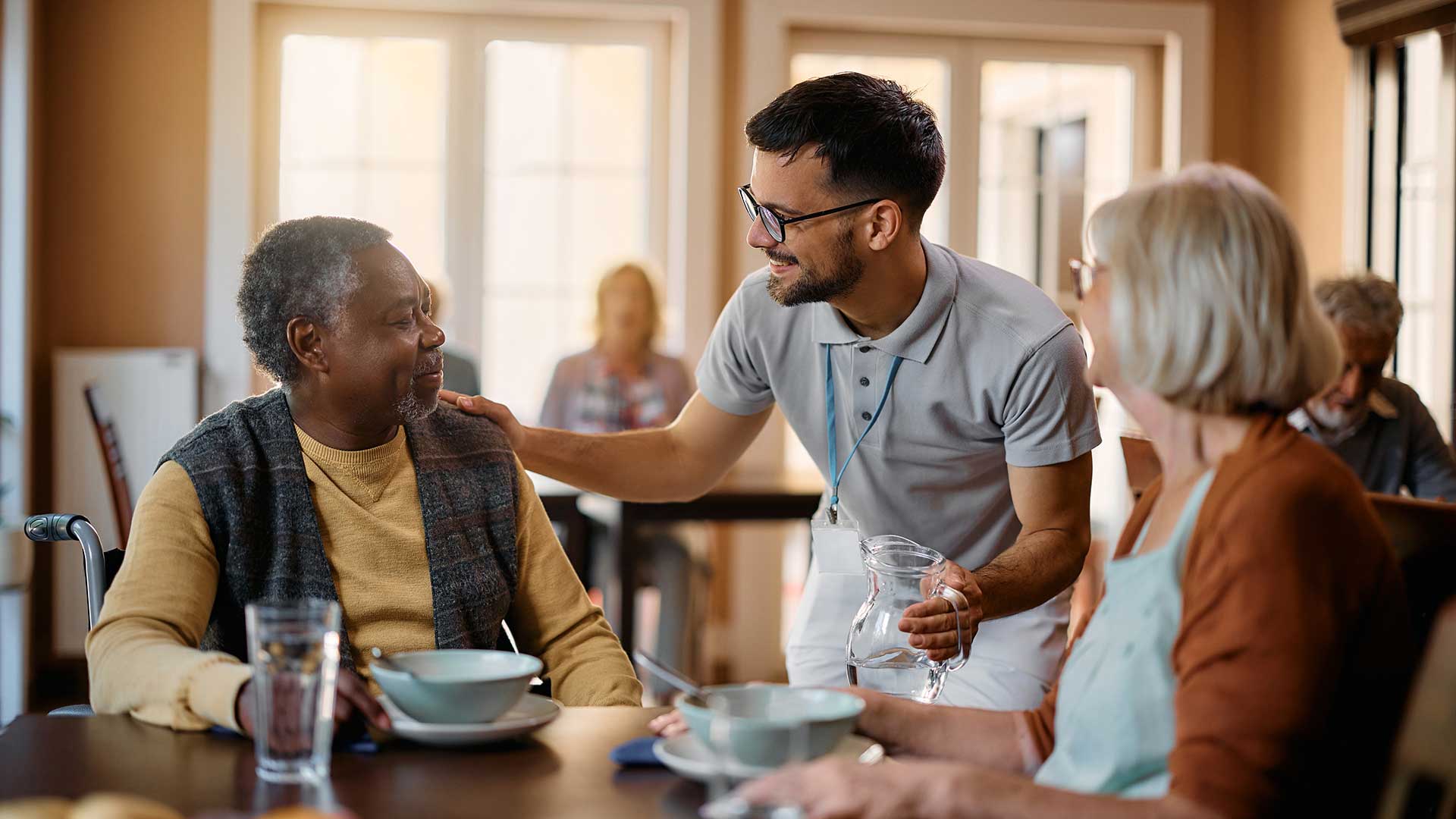 Young healthcare worker talking to seniors during lunch at nursing home.