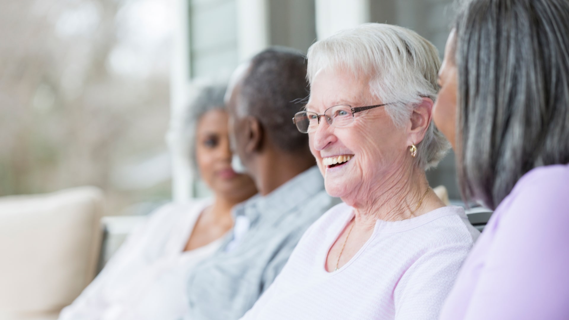 Cheerful senior women talk with one another while sitting on the porch of their retirement home.