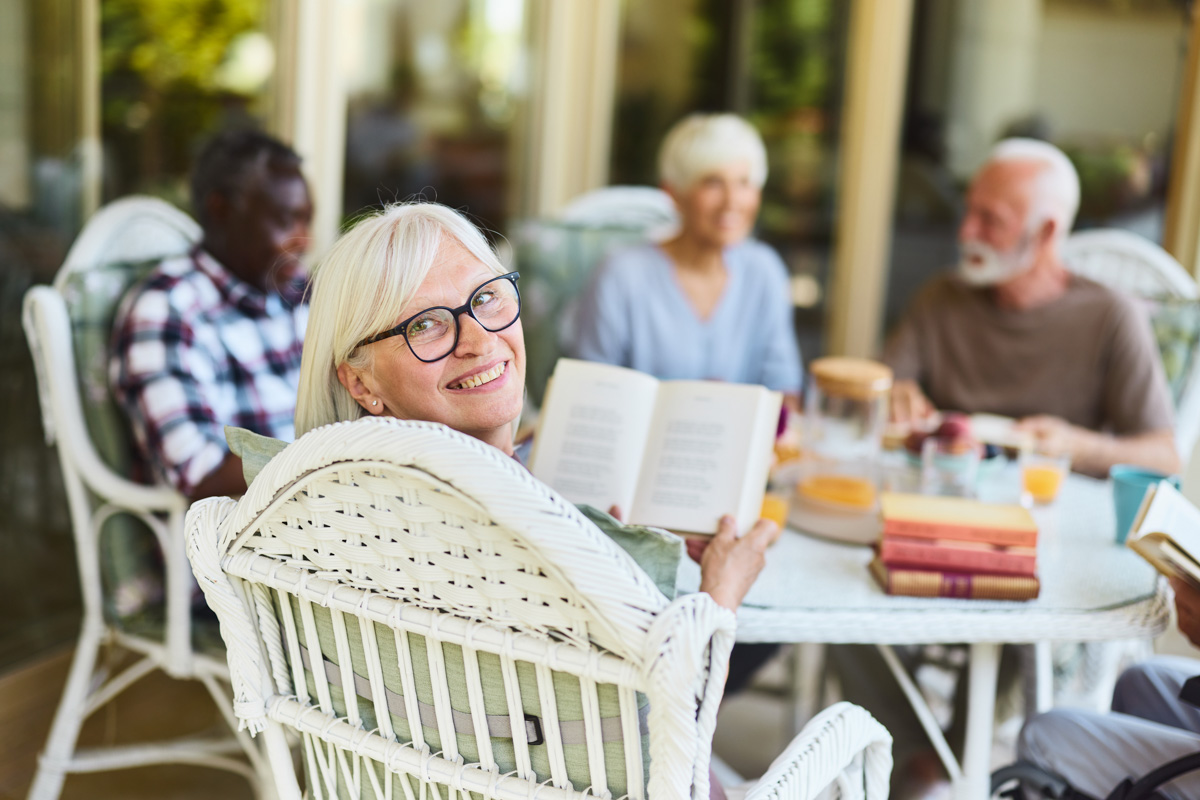 Happy senior woman reading a book with her friends on a patio.