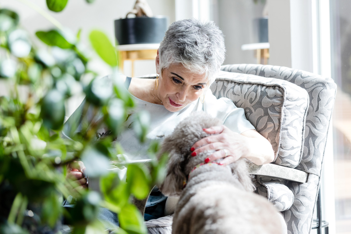 Senior woman sitting in living room looks into dog's face
